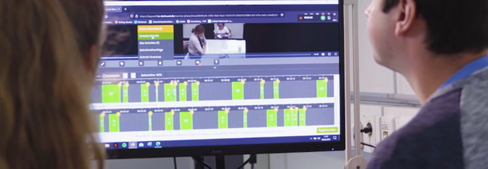 Foto Zwei Studierende sitzen vor einem Bildschirm, auf dem die Lernplattform zu sehen ist